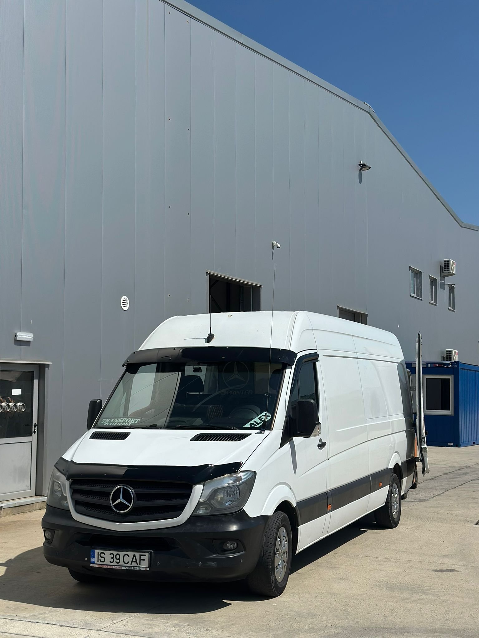 Duba inalta Mercedes Sprinter parcata langa o hala gri cu usile deschise