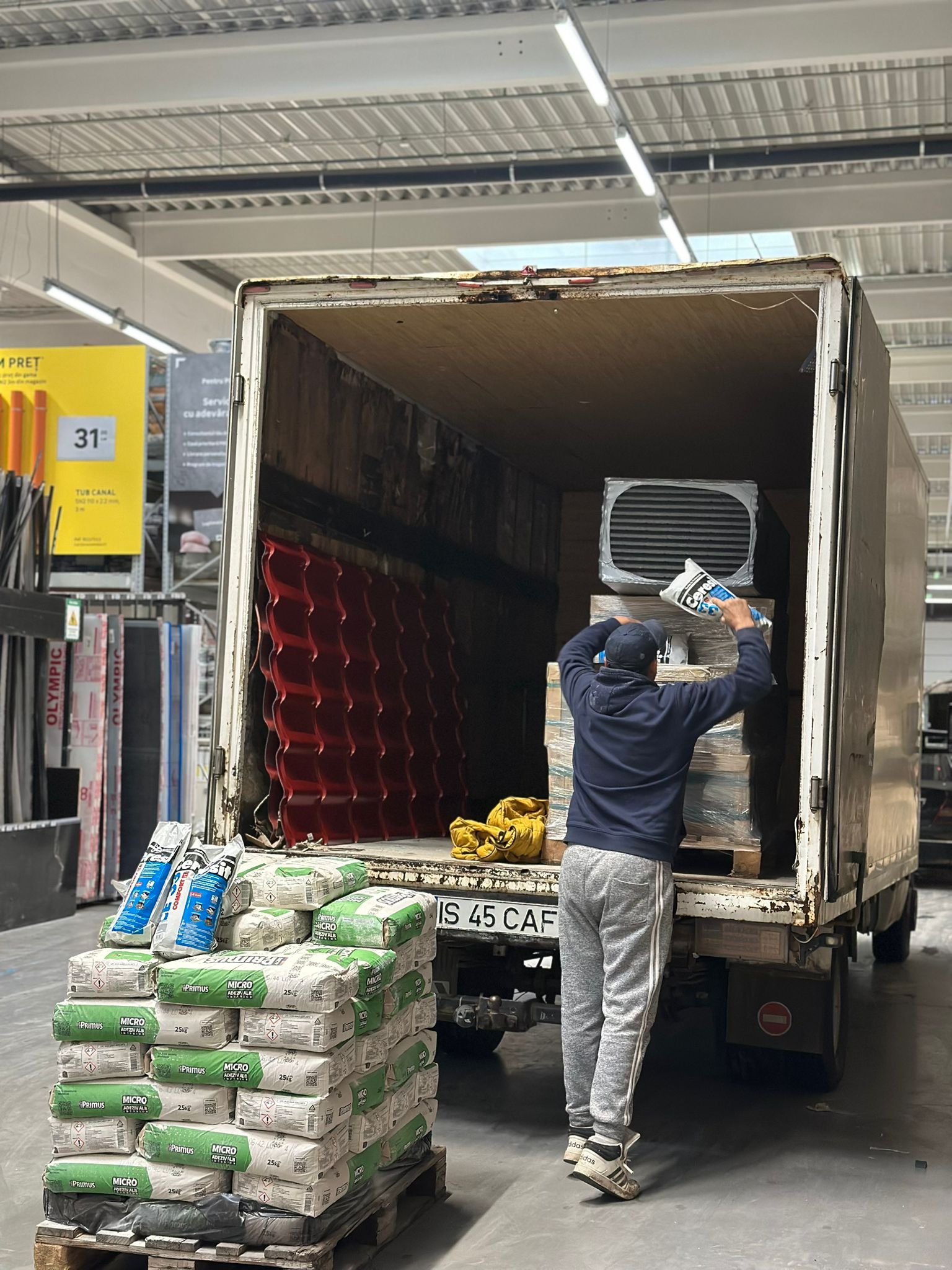 Muncitor asaza saci de adeziv si materiale de constructii in camion la magazin