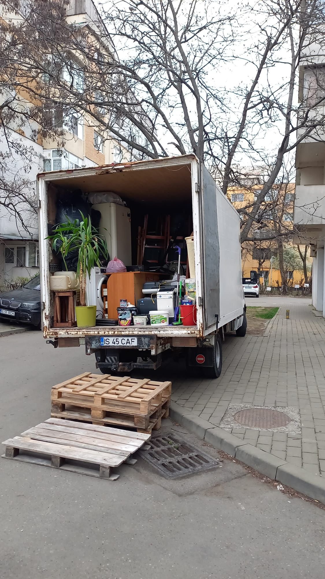 Camion de mutari incarcat cu frigider, mobilier si plante in fata blocului