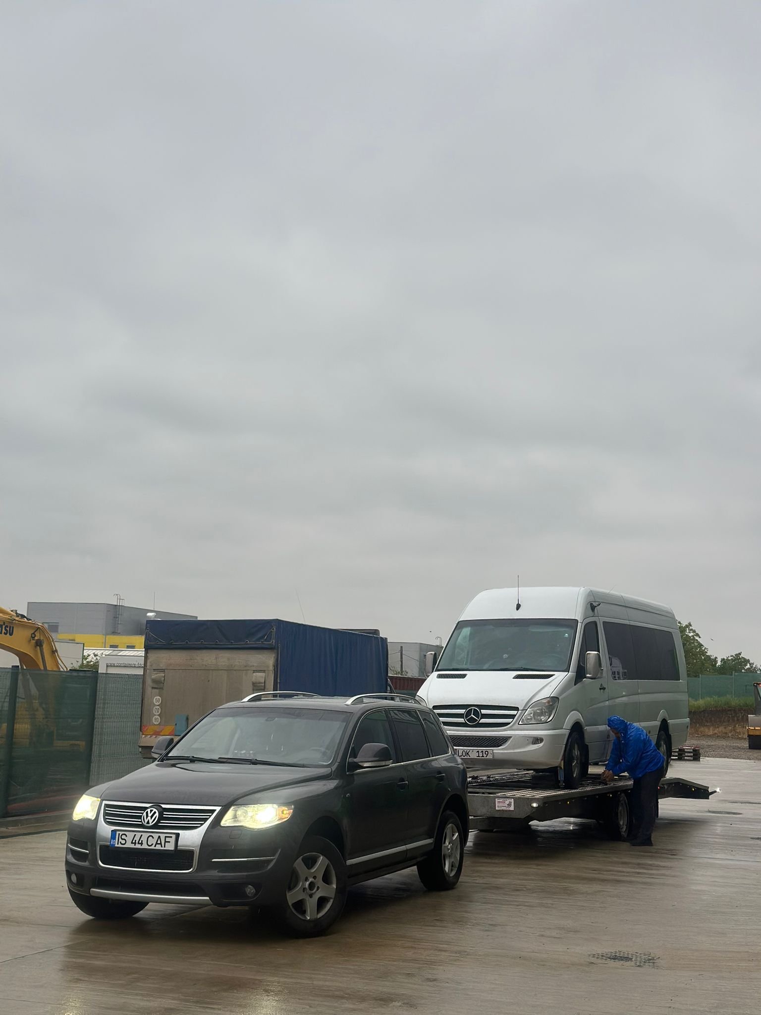 VW Touareg tracteaza un microbuz Sprinter alb pe remorca platforma pe ploaie